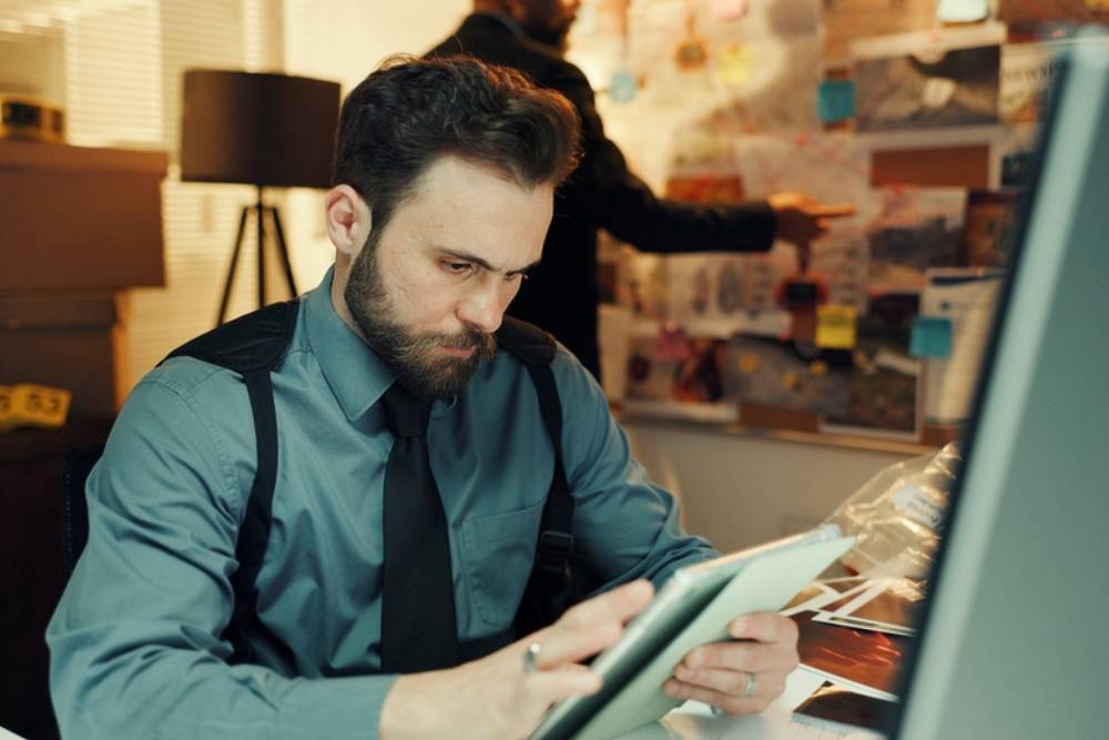 Man, detective or research on tablet in office for arrest warrant, evidence report or online records.